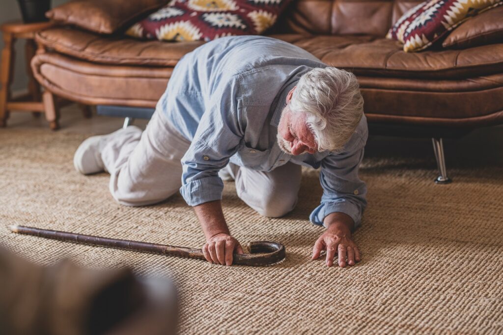 Ein Senior liegt auf dem Boden nach einem Sturz wegen einer Gangstörung. Er stützt sich auf seinen Ellenbogen und einem Gehstock.