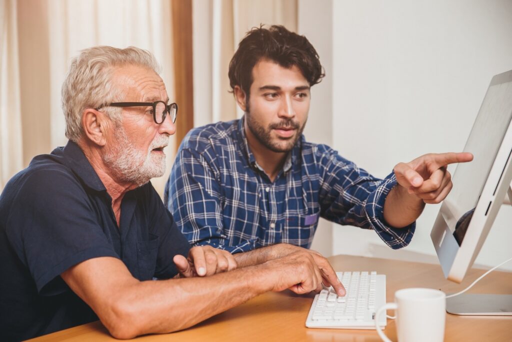 Ein junger Mann hilft einem Senior mit dem Computer.